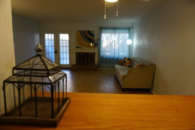 living room with ceiling fan, a brick fireplace, dark wood-type flooring, and french doors