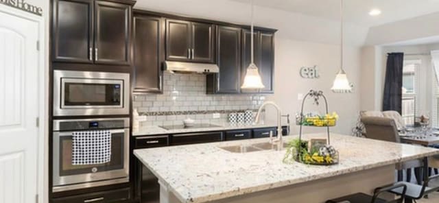 kitchen featuring stainless steel appliances, tasteful backsplash, an island with sink, light stone counters, and sink