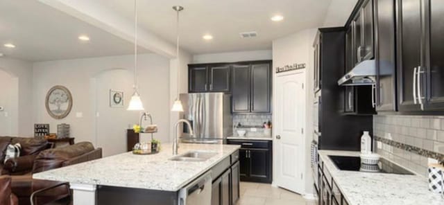 kitchen featuring pendant lighting, a kitchen island with sink, backsplash, appliances with stainless steel finishes, and light tile floors