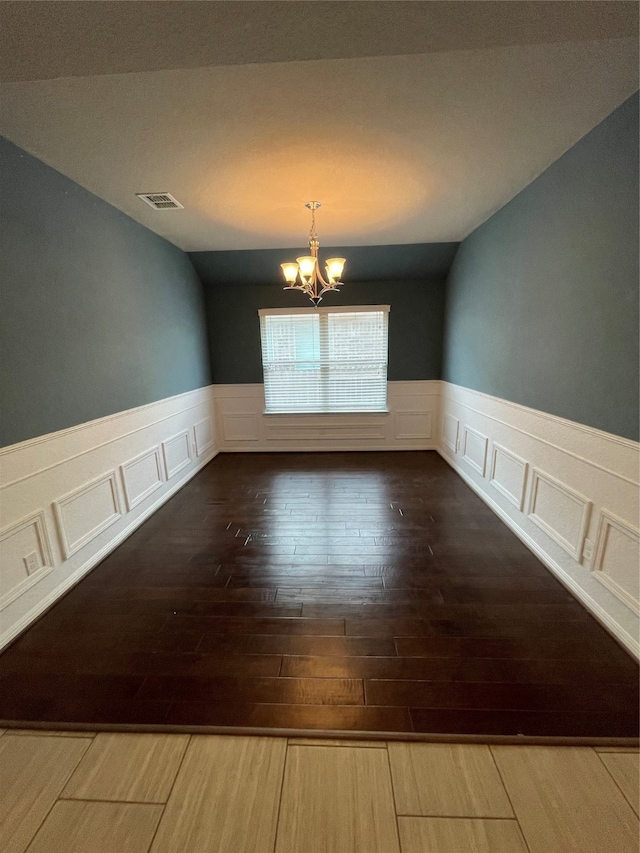 unfurnished room with an inviting chandelier, vaulted ceiling, and hardwood / wood-style floors