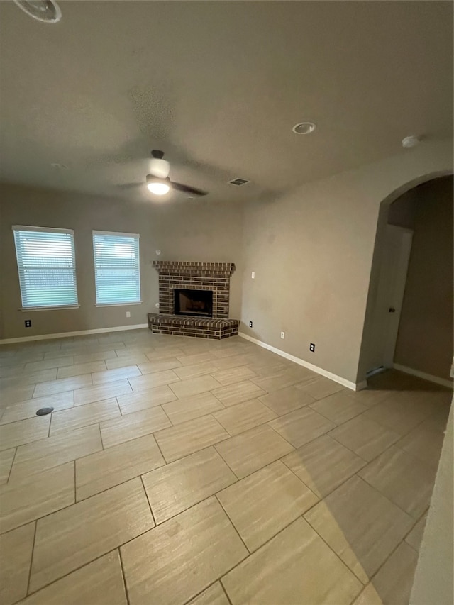 unfurnished living room with ceiling fan, light tile flooring, and a brick fireplace