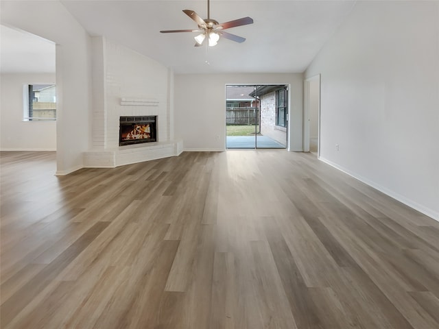 unfurnished living room featuring ceiling fan, lofted ceiling, light wood-type flooring, and a brick fireplace