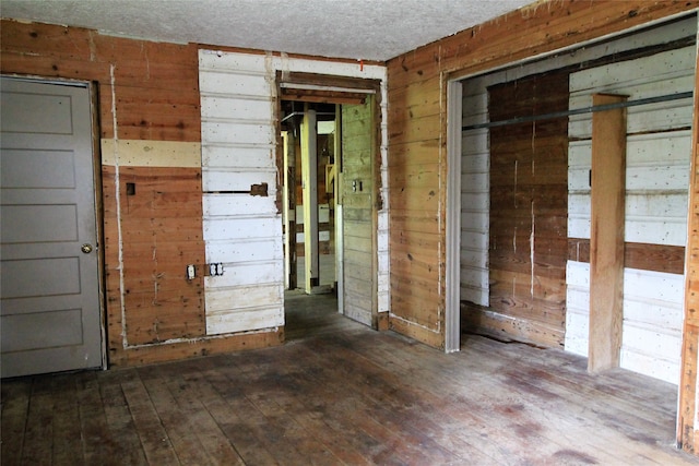 interior space featuring dark wood-type flooring, wood walls, and a textured ceiling