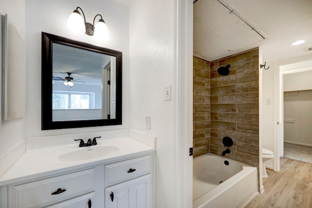 full bathroom featuring vanity, hardwood / wood-style floors, ceiling fan, tiled shower / bath, and toilet