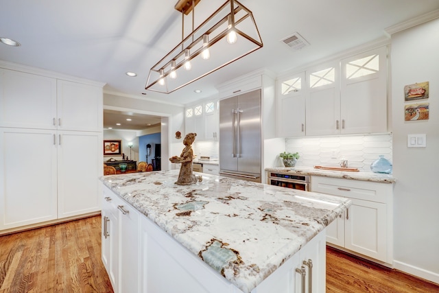 kitchen with light wood-type flooring, stainless steel built in fridge, white cabinets, a center island, and hanging light fixtures