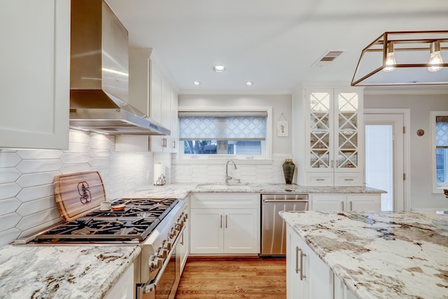 kitchen with stainless steel appliances, sink, wall chimney range hood, pendant lighting, and white cabinetry