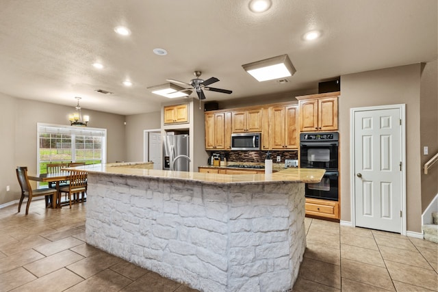 kitchen featuring an island with sink, stainless steel appliances, light tile floors, and ceiling fan with notable chandelier