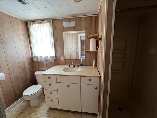 bathroom with tile floors, wood walls, toilet, and vanity