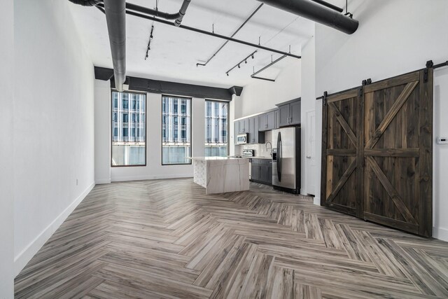 unfurnished living room with a high ceiling, rail lighting, parquet flooring, and a barn door