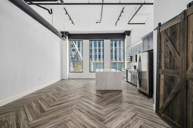 interior space with a high ceiling, a barn door, stainless steel appliances, track lighting, and parquet floors