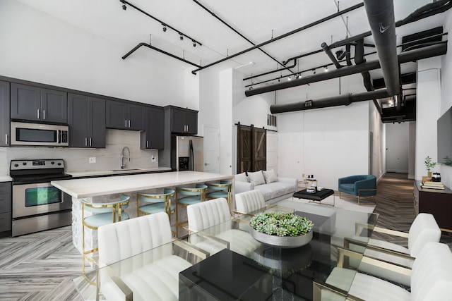 kitchen featuring a high ceiling, stainless steel appliances, a barn door, a center island, and a kitchen breakfast bar