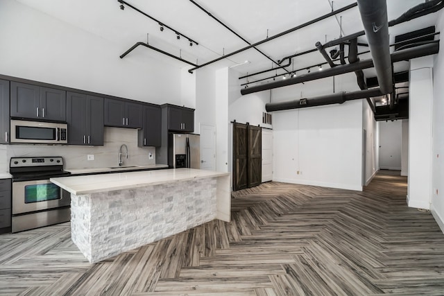 kitchen with rail lighting, a high ceiling, a kitchen island, stainless steel appliances, and parquet floors