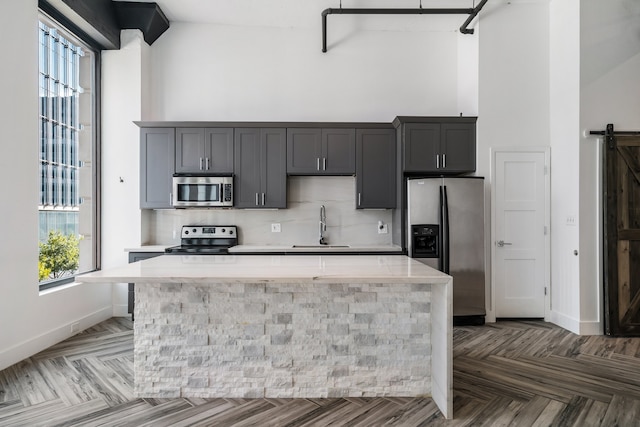 kitchen with tasteful backsplash, dark parquet floors, a barn door, a kitchen island, and appliances with stainless steel finishes