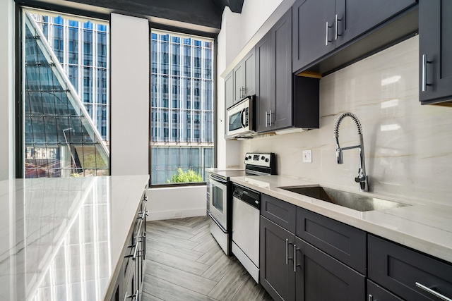 kitchen with light parquet floors, white dishwasher, electric range oven, light stone countertops, and sink