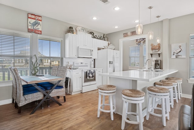 kitchen with white appliances, sink, light hardwood / wood-style floors, decorative light fixtures, and white cabinetry