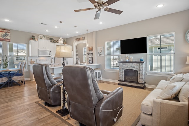 living room with ceiling fan, light hardwood / wood-style flooring, and a stone fireplace