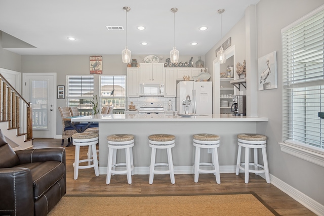 kitchen featuring backsplash, a kitchen breakfast bar, white appliances, and white cabinetry