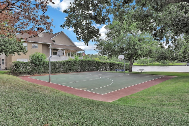 view of sport court with a water view and a lawn