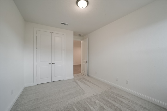 unfurnished bedroom with light colored carpet and a closet