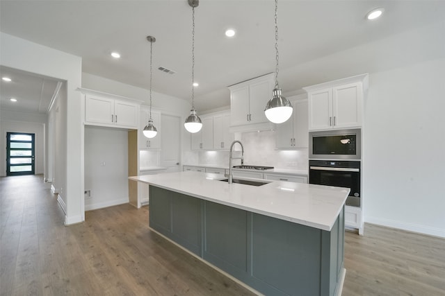 kitchen with white cabinets, pendant lighting, light hardwood / wood-style flooring, a kitchen island with sink, and sink