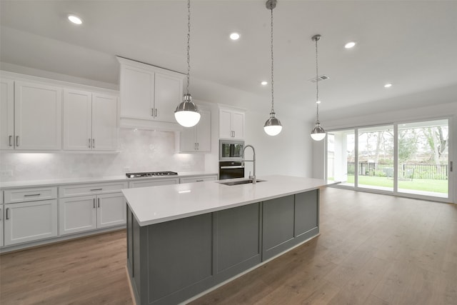 kitchen with stainless steel appliances, white cabinetry, a center island with sink, and sink