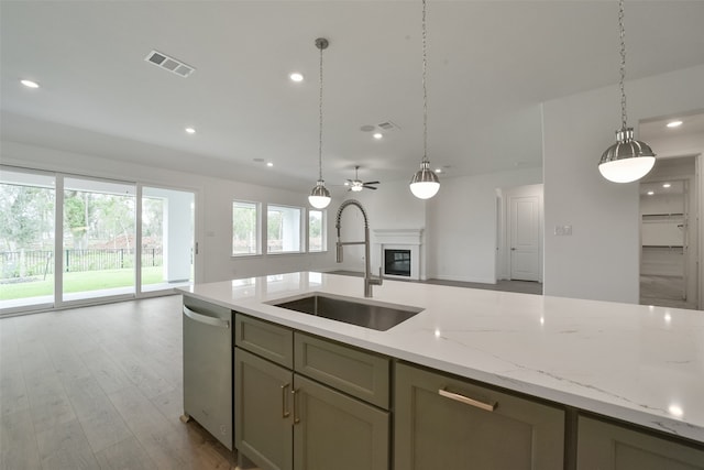 kitchen with light wood-type flooring, dishwasher, light stone counters, sink, and decorative light fixtures