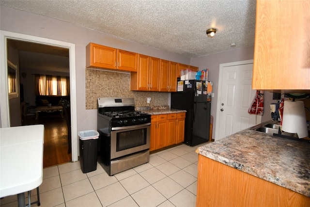 kitchen with a textured ceiling, backsplash, black refrigerator, and gas range