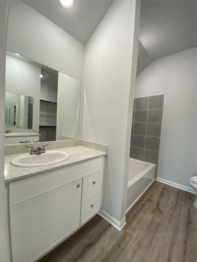 full bathroom with wood finished floors, a bath, vanity, toilet, and baseboards