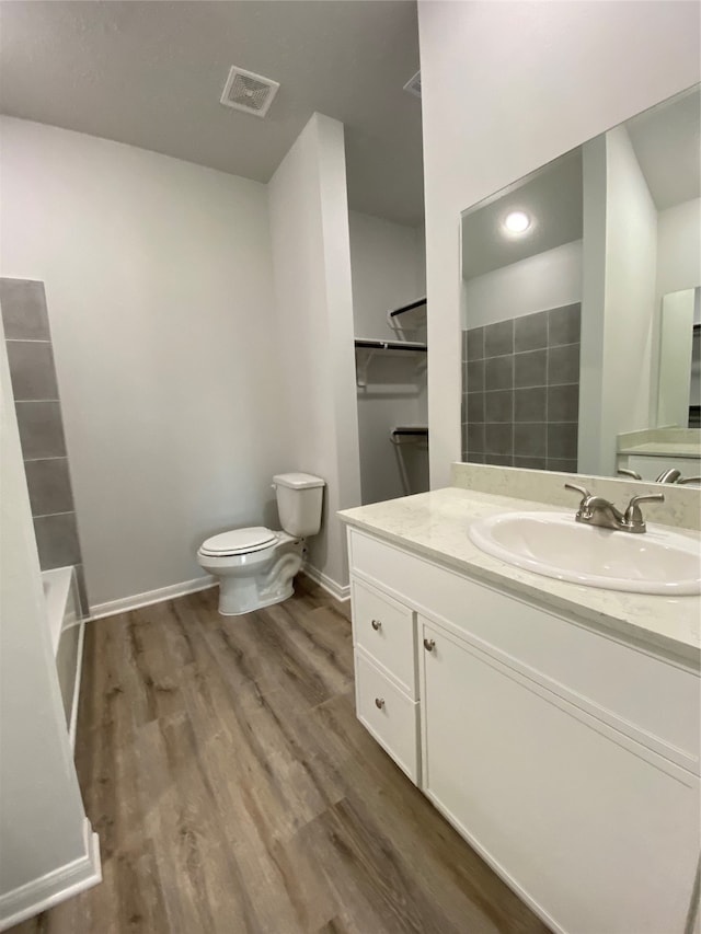 bathroom with toilet, wood finished floors, baseboards, vanity, and a bath