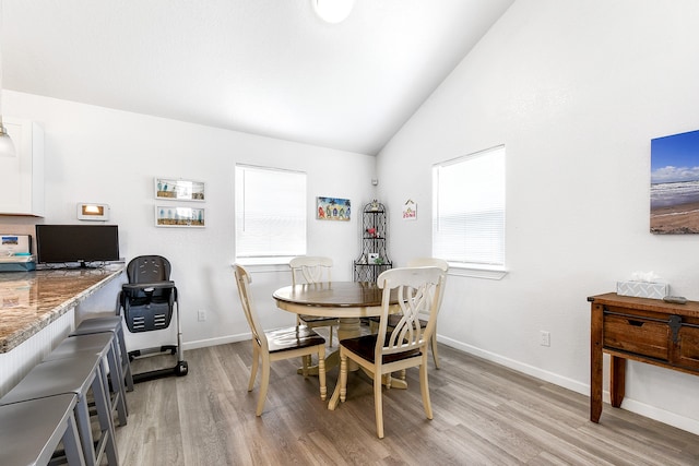 dining space with high vaulted ceiling and light hardwood / wood-style flooring