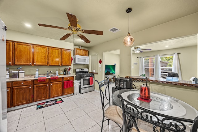 kitchen featuring light tile patterned flooring, gas range, sink, and ceiling fan