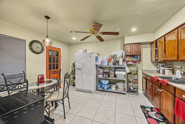 kitchen with white refrigerator with ice dispenser, sink, hanging light fixtures, light tile patterned floors, and ceiling fan