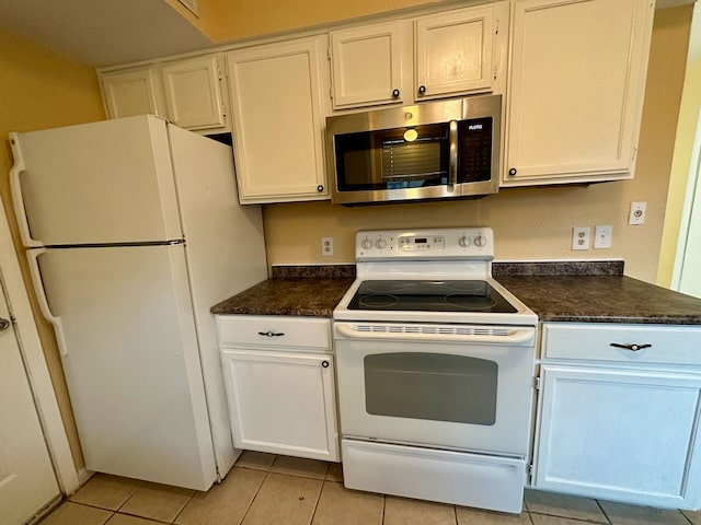 kitchen with white cabinets, light tile floors, white appliances, and dark stone counters