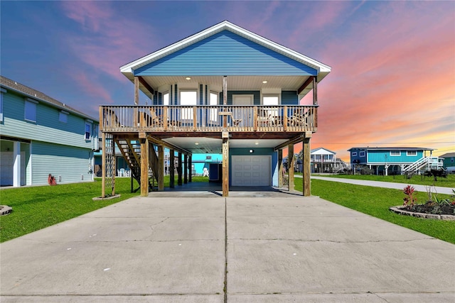 raised beach house featuring covered porch, a front yard, a carport, concrete driveway, and an attached garage