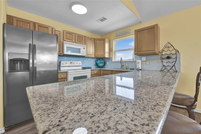 kitchen with light stone countertops, backsplash, white appliances, a textured ceiling, and hardwood / wood-style flooring