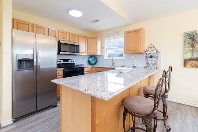 kitchen featuring visible vents, light brown cabinetry, appliances with stainless steel finishes, a peninsula, and light wood-style flooring