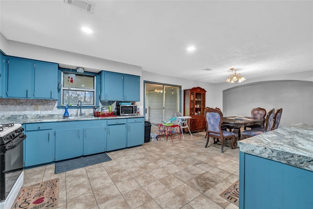 kitchen with a notable chandelier, blue cabinets, gas stove, backsplash, and sink