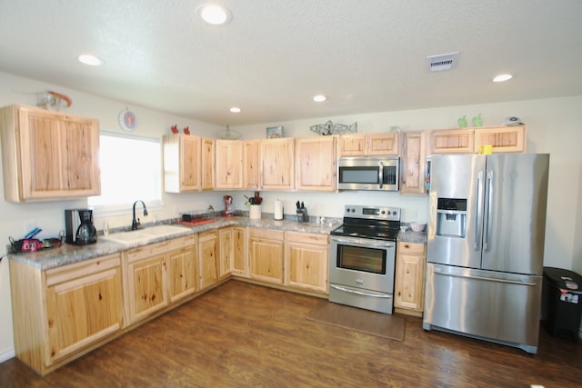 kitchen with light stone counters, appliances with stainless steel finishes, light brown cabinetry, sink, and dark wood-type flooring