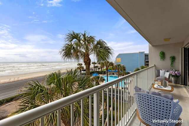 balcony with a water view, a community pool, and a beach view