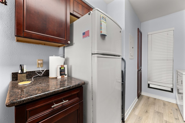 kitchen featuring white fridge, dark stone counters, and light wood-type flooring