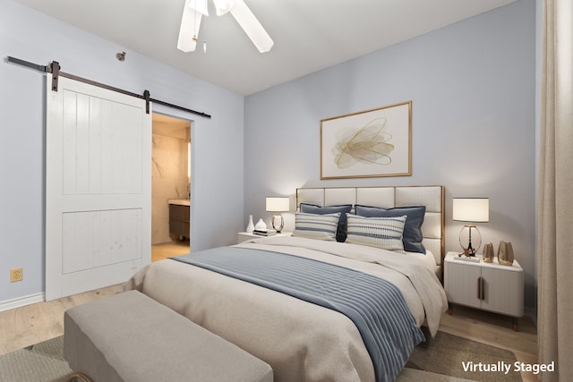 bedroom featuring ensuite bath, a barn door, ceiling fan, and light hardwood / wood-style flooring