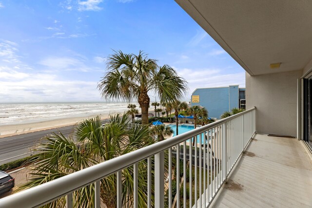 balcony with a water view, a beach view, and a community pool