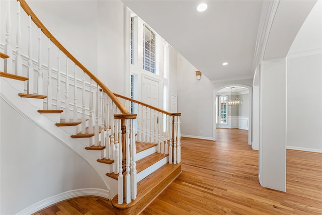 staircase with crown molding, hardwood / wood-style floors, and an inviting chandelier