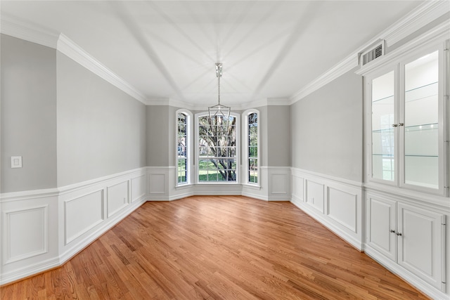 unfurnished dining area featuring ornamental molding, a chandelier, and light hardwood / wood-style flooring