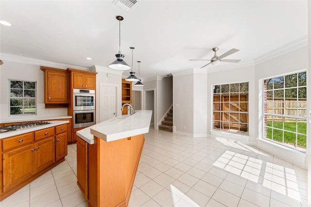 kitchen featuring sink, ornamental molding, pendant lighting, appliances with stainless steel finishes, and a center island with sink