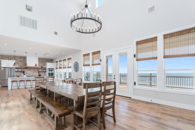 dining area featuring light hardwood / wood-style floors, a high ceiling, brick wall, a water view, and a chandelier