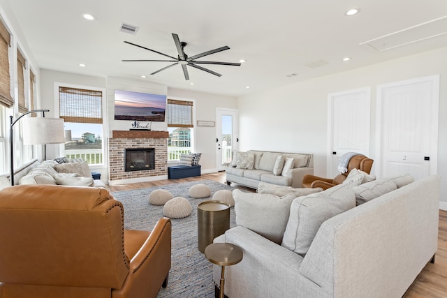 living room featuring a brick fireplace, ceiling fan, and light wood-type flooring