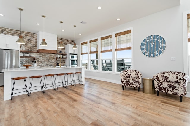 kitchen with appliances with stainless steel finishes, decorative light fixtures, an island with sink, light hardwood / wood-style flooring, and white cabinets