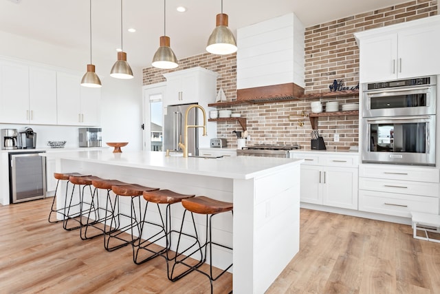 kitchen with stainless steel appliances, pendant lighting, an island with sink, white cabinets, and beverage cooler