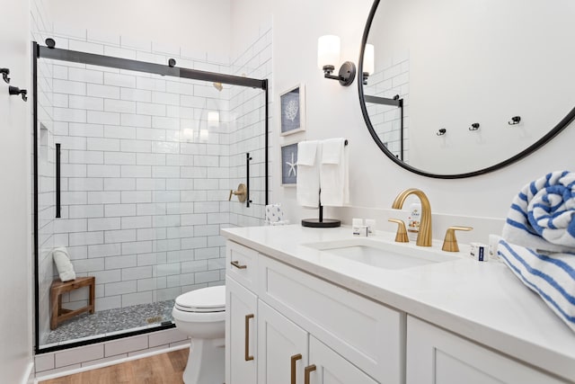 bathroom featuring wood-type flooring, vanity, toilet, and a shower with shower door